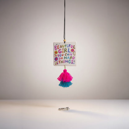 Patchwork with Busyfingers air freshener with colorful text 'Beautiful Girl, You Can Do Hard Things' and pink and teal tassels.