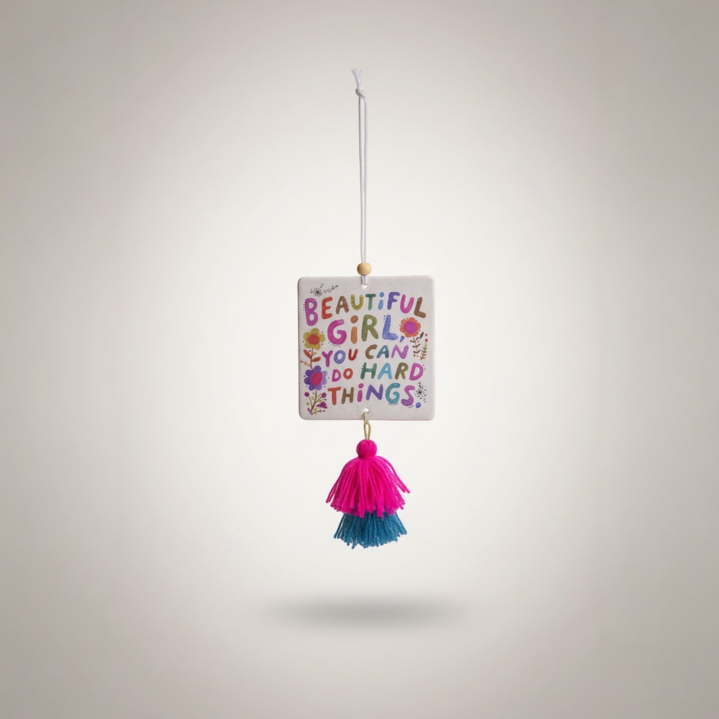 Patchwork with Busyfingers air freshener with colorful text 'BEAUTIFUL GIRL YOU CAN DO HARD THINGS' and floral design, featuring pink and teal tassels.