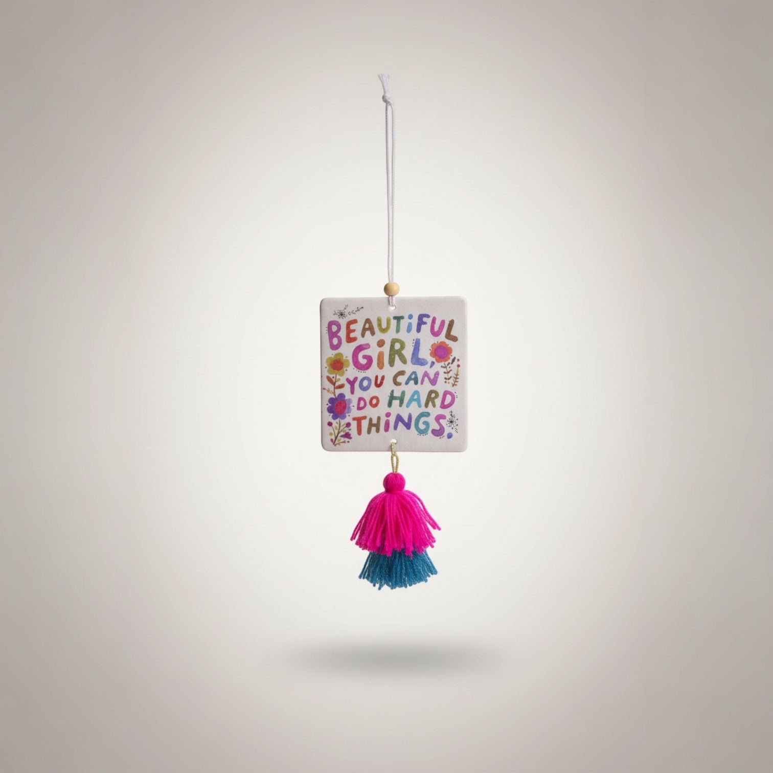 Patchwork with Busyfingers air freshener with colorful text 'BEAUTIFUL GIRL YOU CAN DO HARD THINGS' and floral design, featuring pink and teal tassels.