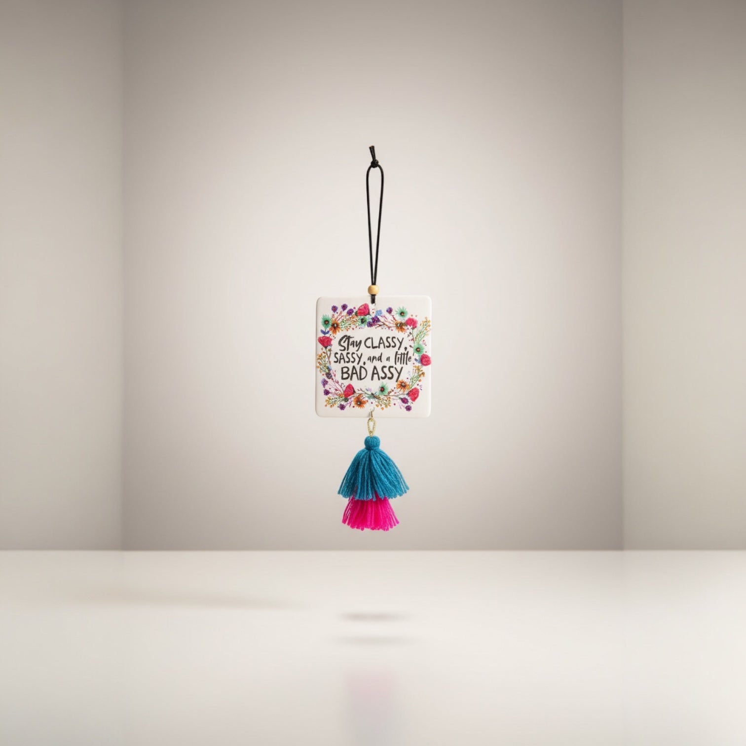 Patchwork with Busyfingers square air freshener with floral border and text 'Stay Classy Sassy, and a little BAD ASSY'. Features teal and pink tassels.