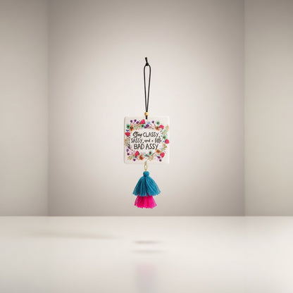 Patchwork with Busyfingers square air freshener with floral border and text 'Stay Classy Sassy, and a little BAD ASSY'. Features teal and pink tassels.
