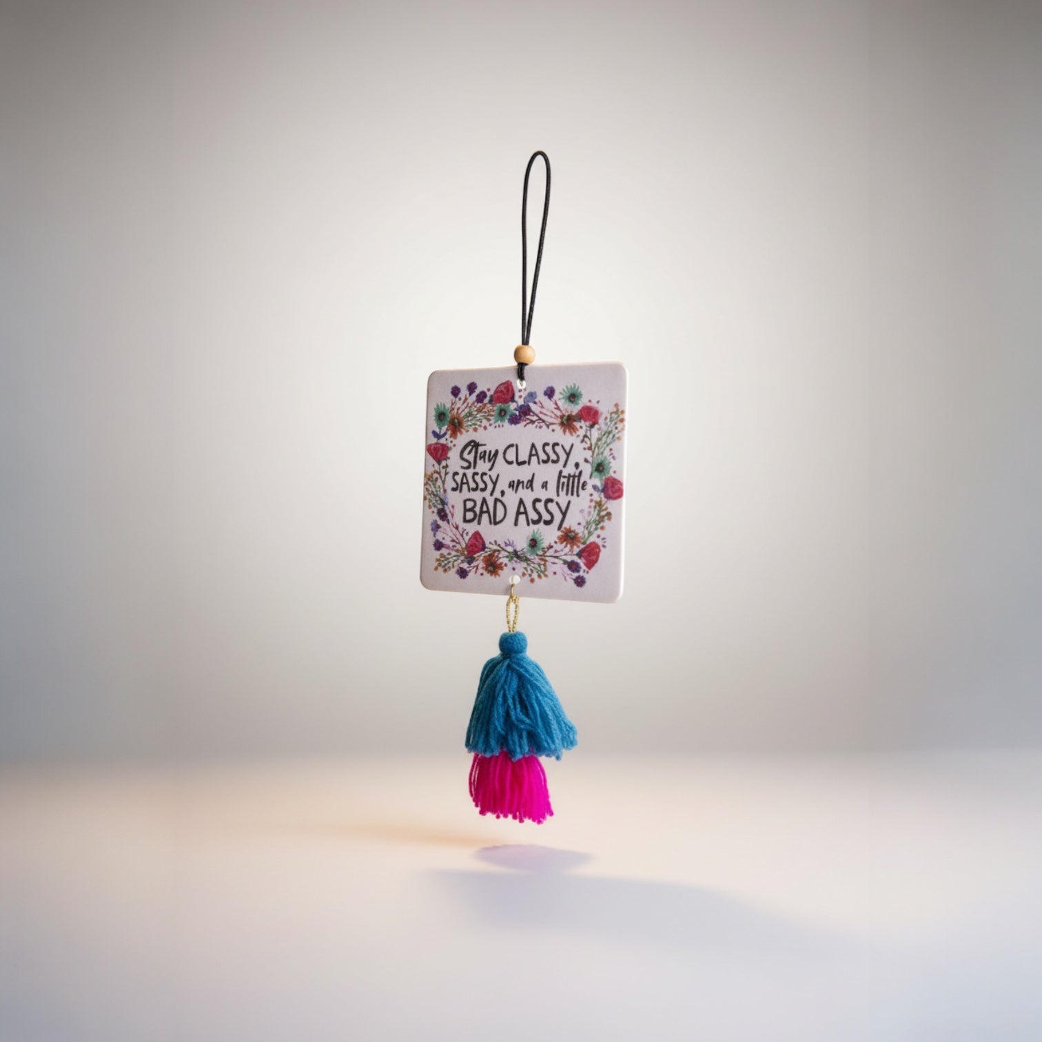 Patchwork with Busyfingers air freshener with floral design and text 'Stay Classy, Sassy, and a little BAD ASSY', featuring blue and pink tassels.