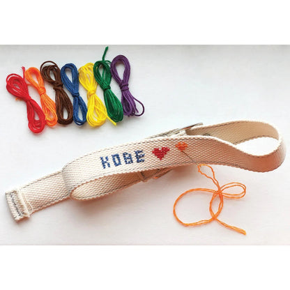 Patchwork with Busyfingers DIY cross stitch dog collar kit with rainbow threads and needle. Features a cream canvas collar with 'KOBE' and a red heart stitched on.