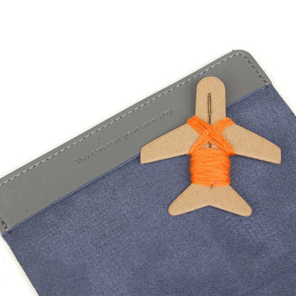 Patchwork with Busyfingers grey faux leather passport holder with orange embroidery thread on a wooden airplane.