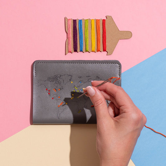Patchwork with Busyfingers grey faux leather passport holder with world map design, being embroidered with colorful threads.