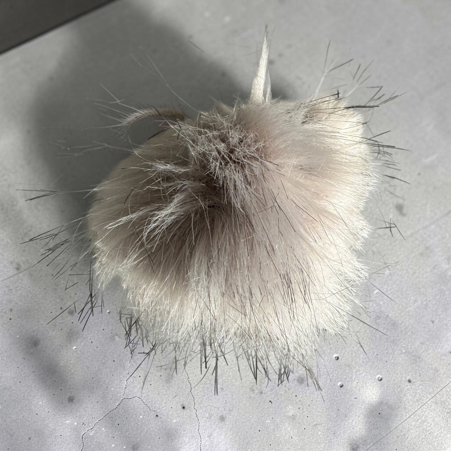 Patchwork with Busyfingers plush faux fur beanie pom pom in a soft beige tone with long wispy dark-tipped fibers.