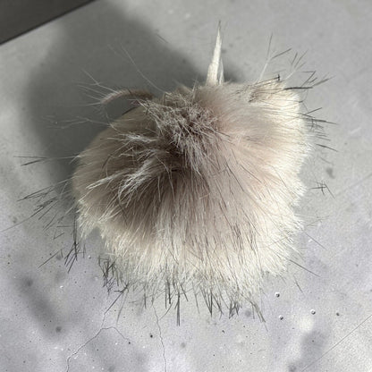 Patchwork with Busyfingers plush faux fur beanie pom pom in a soft beige tone with long wispy dark-tipped fibers.