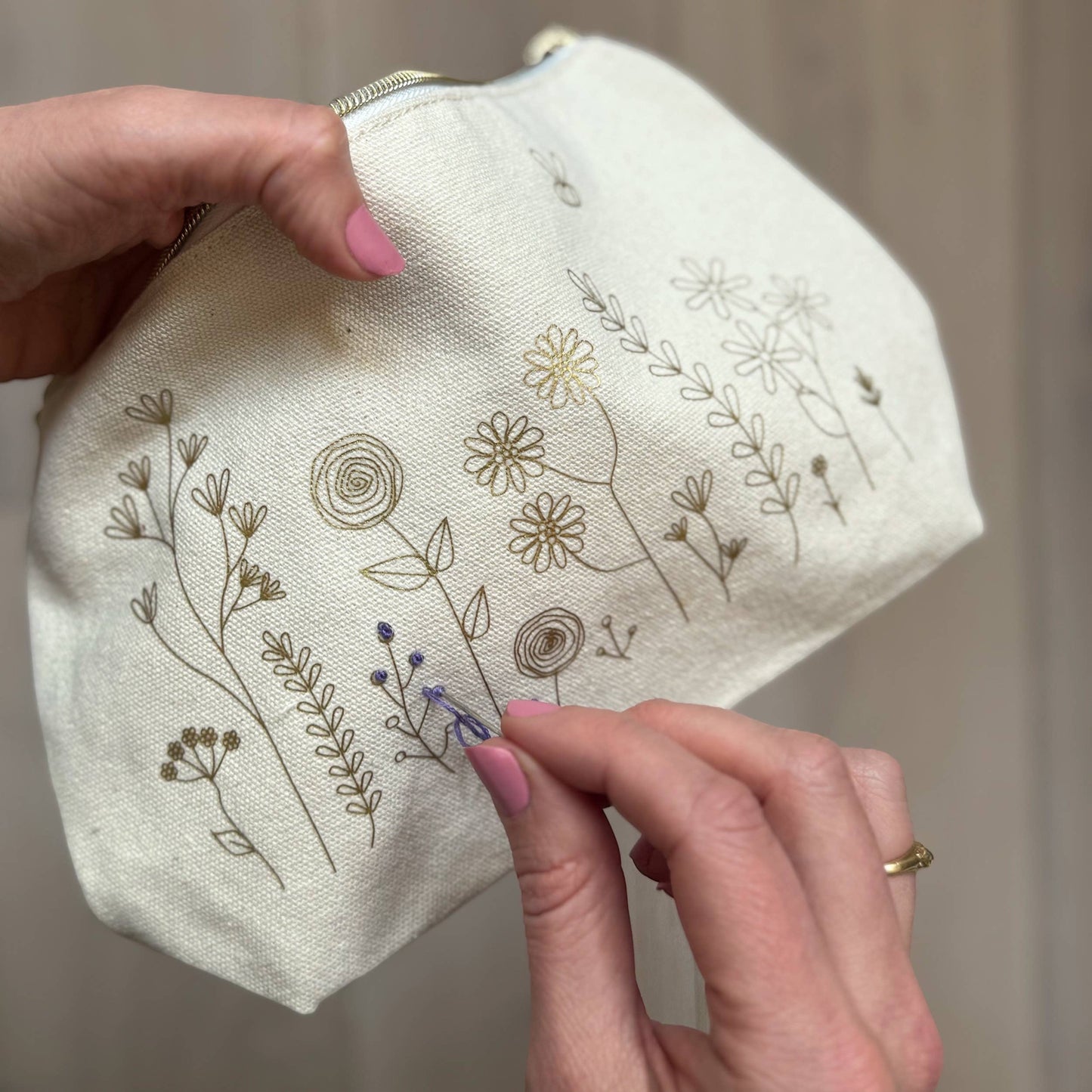 Patchwork with Busyfingers floral embroidery kit on a canvas zip pouch with gold and purple thread.