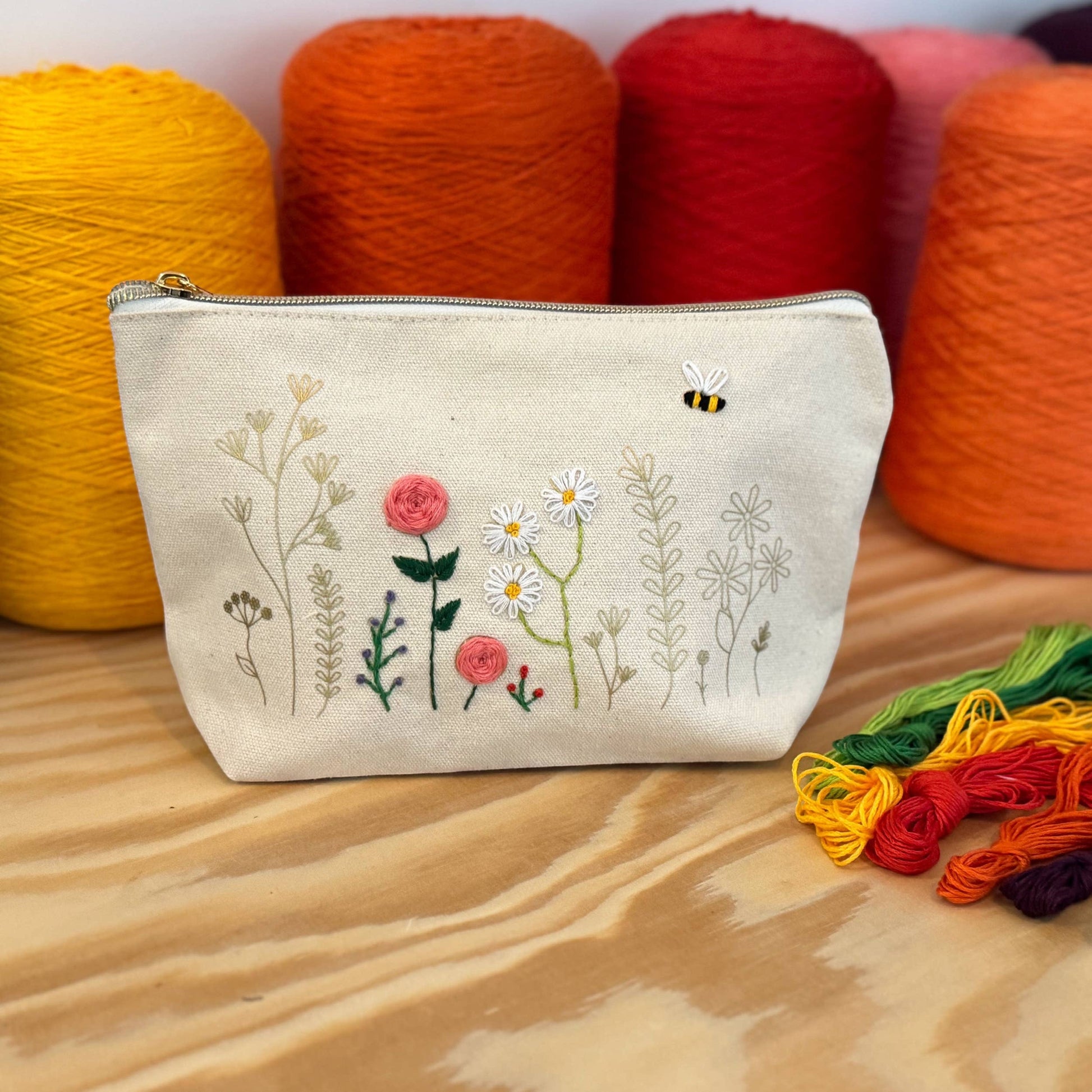 Patchwork with Busyfingers floral embroidery kit on a canvas pouch with pink roses, daisies, and a bee.