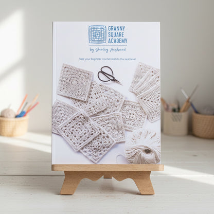 Patchwork with Busyfingers Granny Square Academy crochet instruction book on a wooden stand with yarn and hooks