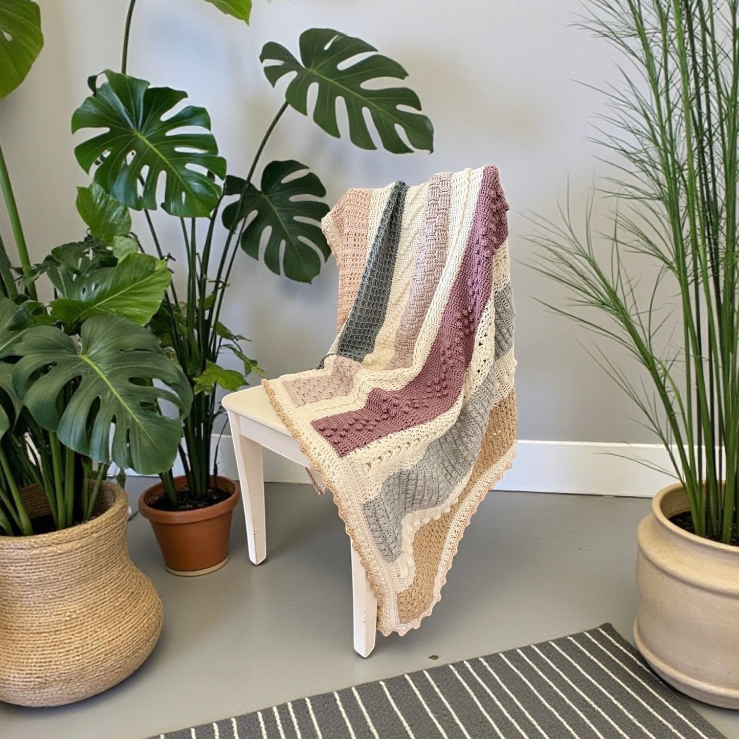 Patchwork with Busyfingers Hidden Stitch yarn set in cream, natural, petal, sand, moss, dusty pink, and light grey. Crochet blanket draped over a white chair.