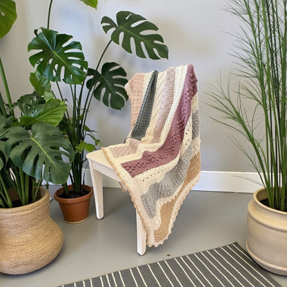 Patchwork with Busyfingers Hidden Stitch yarn set in cream, natural, petal, sand, moss, dusty pink, and light grey. Crochet blanket draped over a white chair.