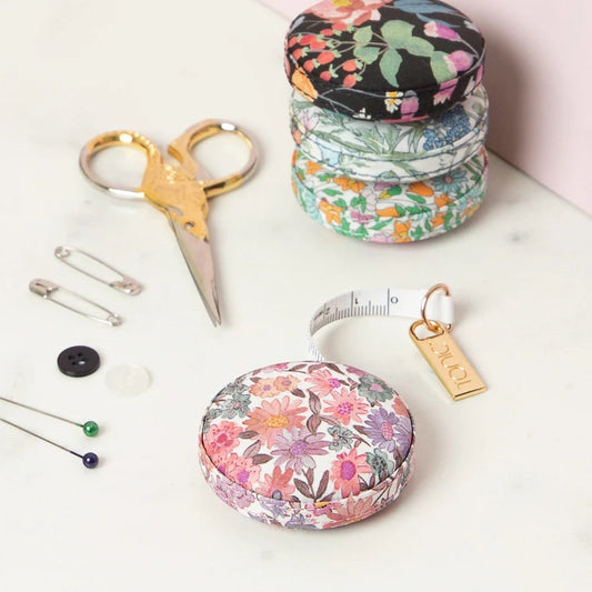 Patchwork with Busyfingers Liberty Tana Lawn floral measuring tape with gold tab, next to sewing notions.