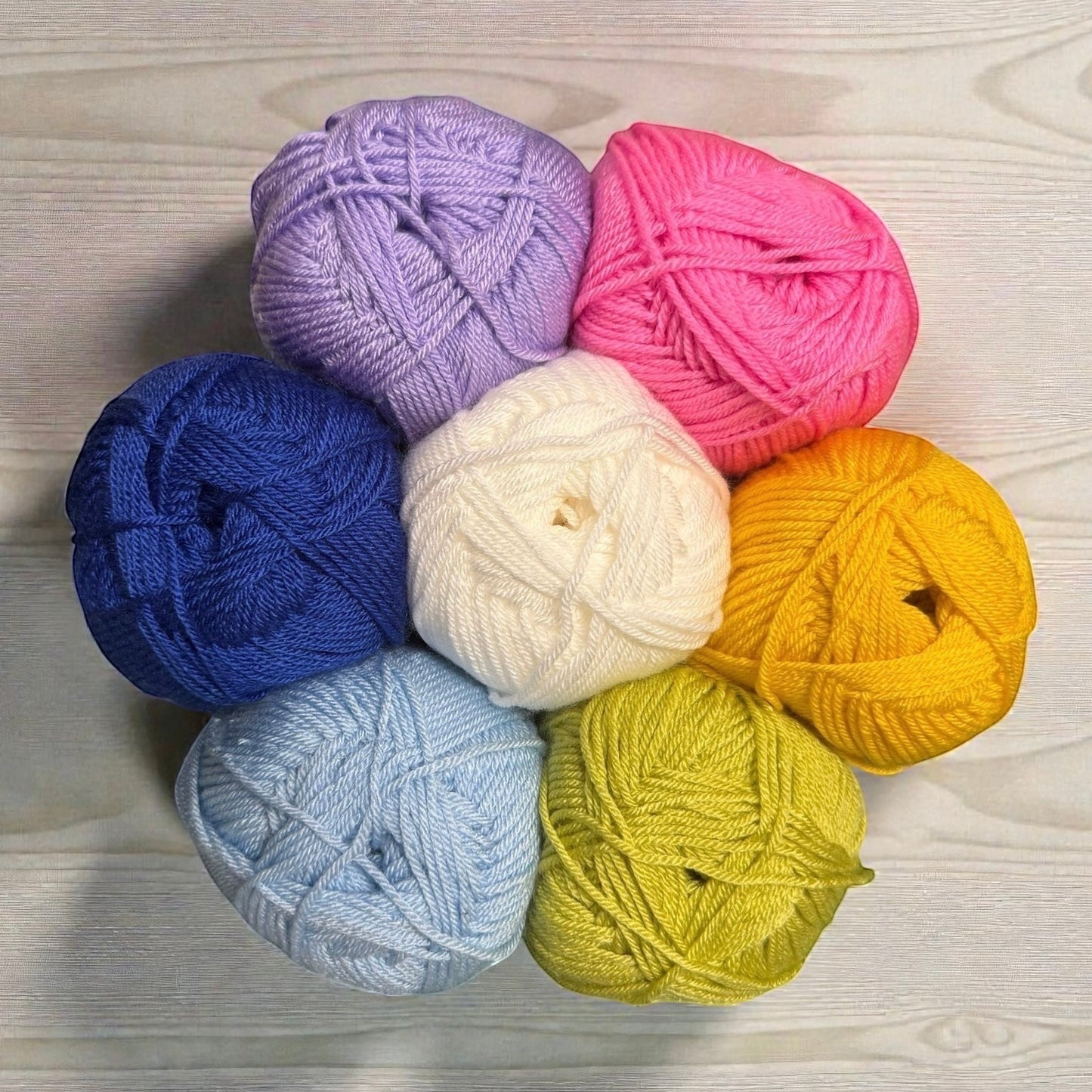 Patchwork with Busyfingers yarn set for Hidden Stitch Blanket CAL: purple, pink, white, yellow, blue, light blue, and lime green yarn balls arranged in a flower shape.