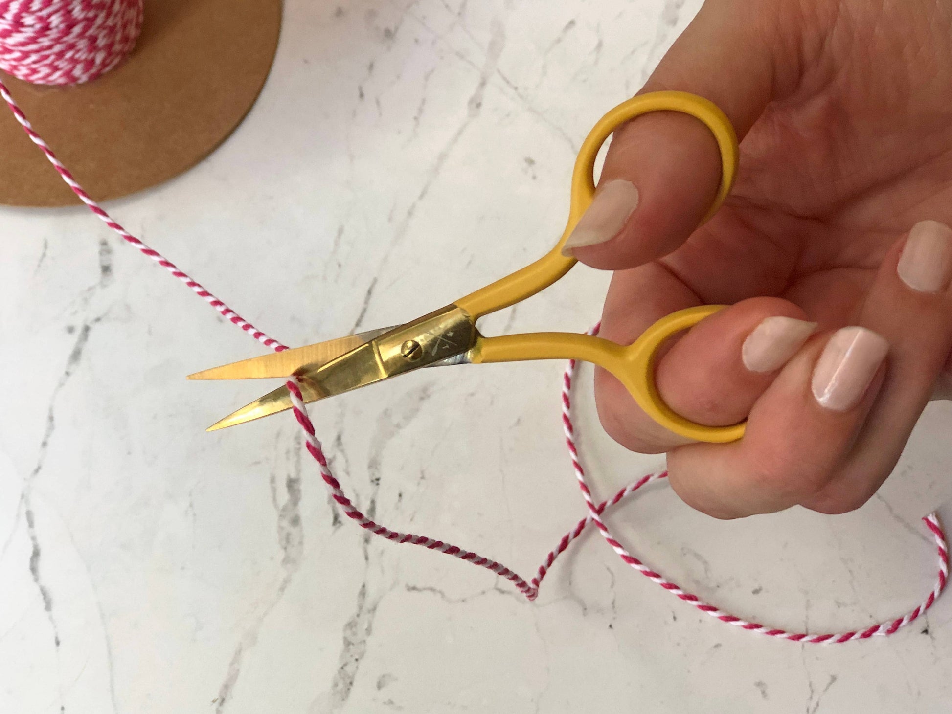 Patchwork with Busyfingers yellow embroidery scissors with gold finish blades cutting pink and white twine.